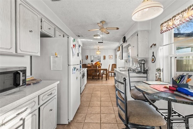 kitchen with stainless steel microwave, light countertops, range with electric stovetop, freestanding refrigerator, and a textured ceiling