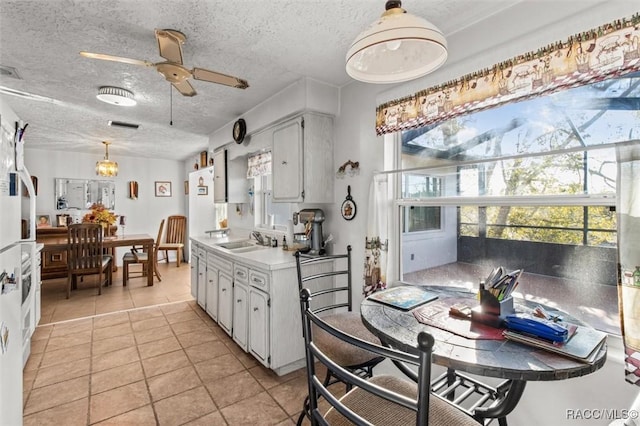 kitchen with a textured ceiling, hanging light fixtures, light tile patterned floors, and a sink