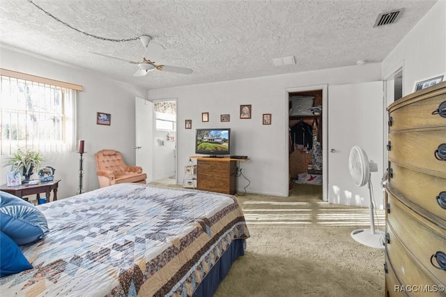 bedroom featuring visible vents, a walk in closet, a textured ceiling, carpet floors, and ceiling fan