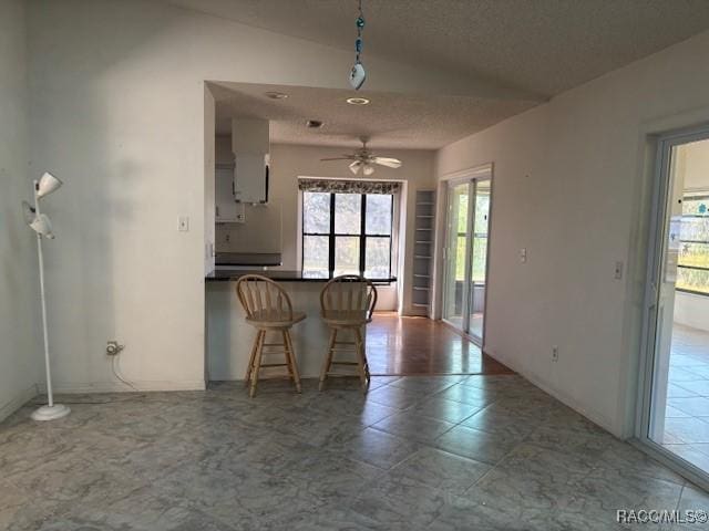 kitchen with ceiling fan, a breakfast bar area, kitchen peninsula, and a textured ceiling