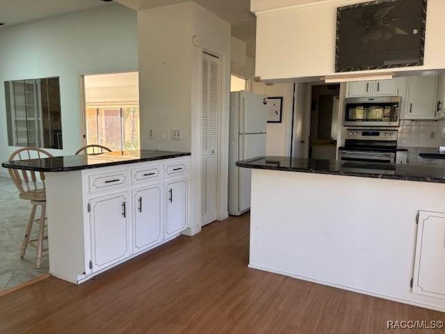 kitchen with stainless steel appliances, dark hardwood / wood-style floors, white cabinets, a kitchen bar, and kitchen peninsula