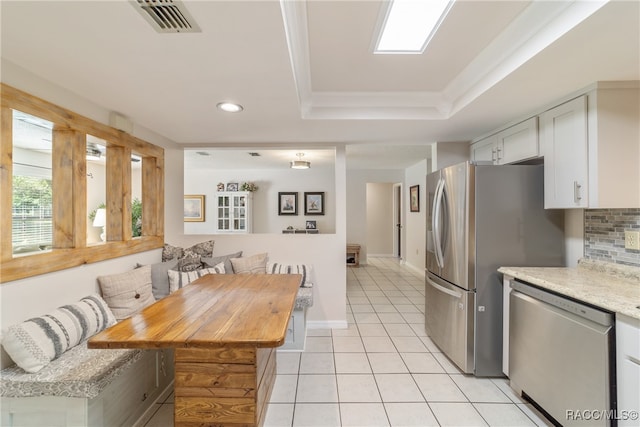 kitchen with decorative backsplash, appliances with stainless steel finishes, breakfast area, light tile patterned floors, and white cabinets