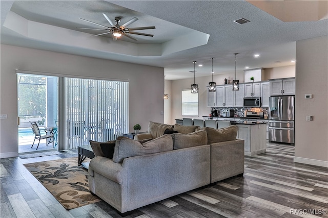 living room featuring a tray ceiling, ceiling fan, a textured ceiling, and dark hardwood / wood-style floors