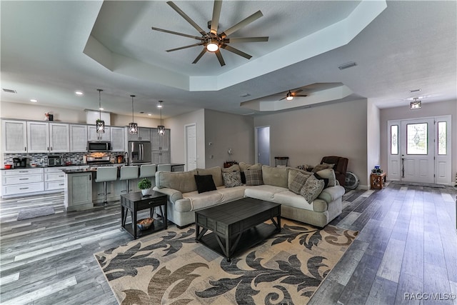 living room featuring a raised ceiling, ceiling fan, and dark hardwood / wood-style floors