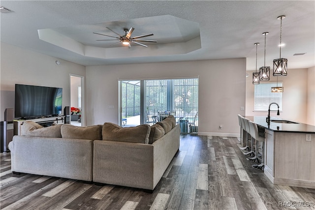 living room featuring dark hardwood / wood-style floors, a raised ceiling, sink, and ceiling fan with notable chandelier