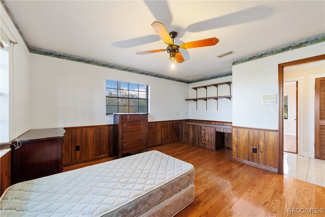 bedroom featuring ceiling fan, wood walls, and light wood-type flooring