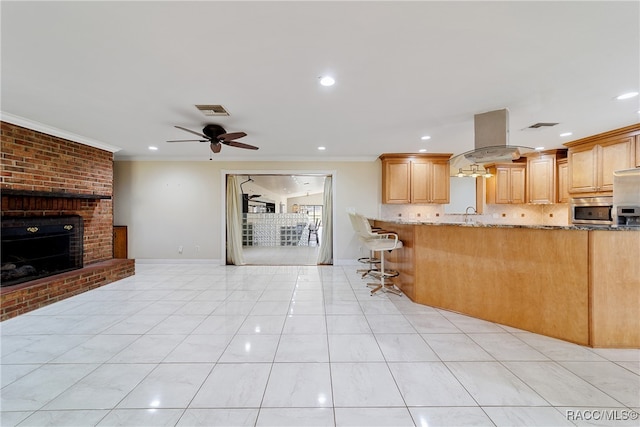 kitchen with stone counters, light brown cabinetry, a kitchen bar, and island range hood