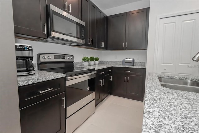 kitchen with sink, light stone countertops, light tile patterned floors, dark brown cabinets, and stainless steel appliances