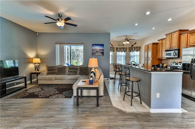 kitchen with a breakfast bar, ceiling fan, appliances with stainless steel finishes, and light hardwood / wood-style flooring