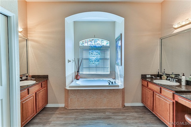 bathroom with hardwood / wood-style floors, vanity, and tiled tub