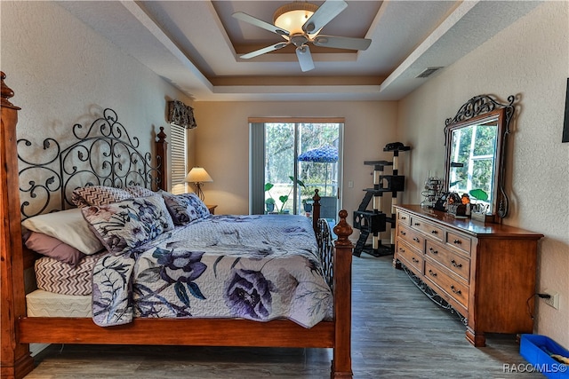 bedroom featuring multiple windows, dark hardwood / wood-style flooring, a raised ceiling, and ceiling fan