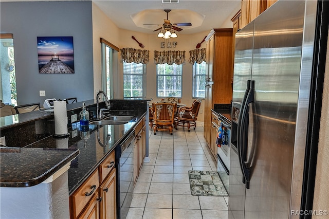 kitchen featuring appliances with stainless steel finishes, ceiling fan, sink, light tile patterned floors, and dark stone countertops