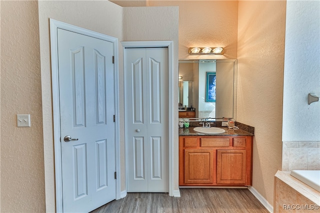 bathroom with tiled tub, hardwood / wood-style floors, and vanity