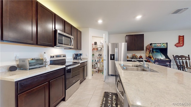 kitchen with sink, light stone countertops, light tile patterned floors, dark brown cabinetry, and stainless steel appliances