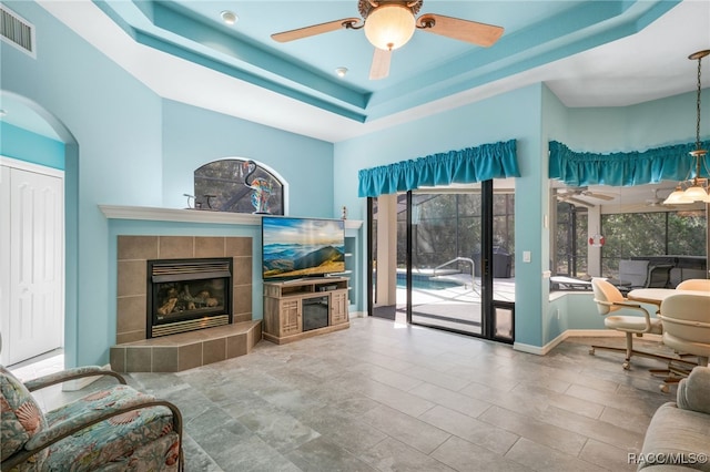 living room with ceiling fan, a fireplace, and a tray ceiling