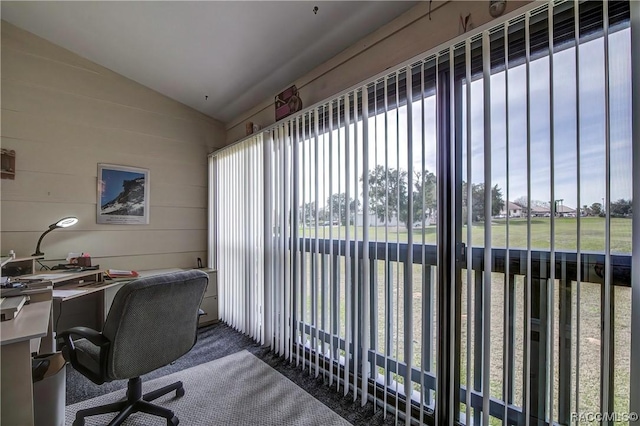 carpeted home office featuring vaulted ceiling and wood walls