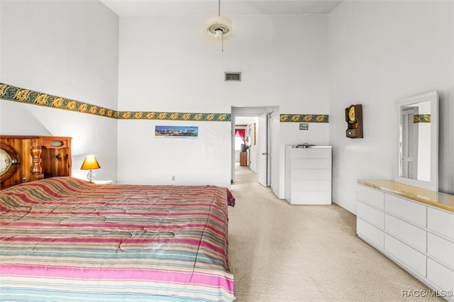 bedroom with visible vents, light carpet, and a high ceiling