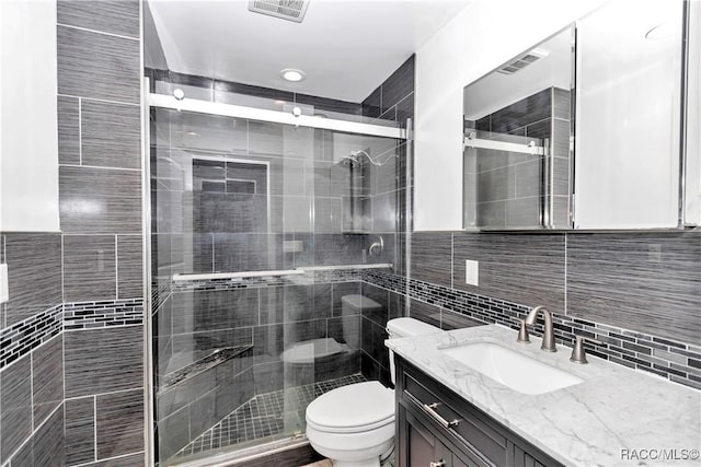 bathroom with vanity, a shower with door, decorative backsplash, toilet, and tile walls