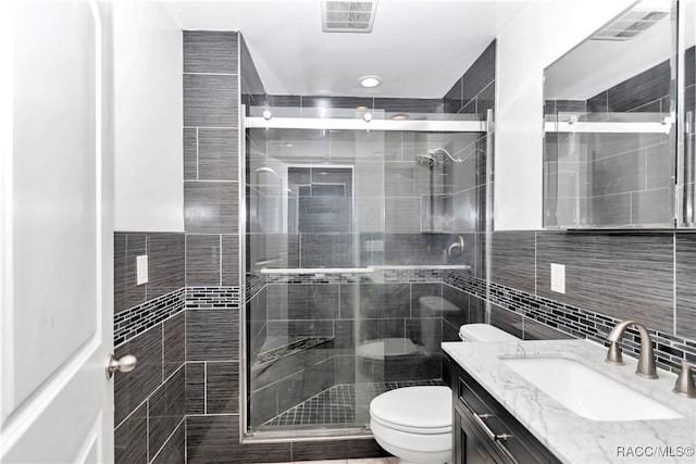 bathroom with toilet, a shower with shower door, and tile walls