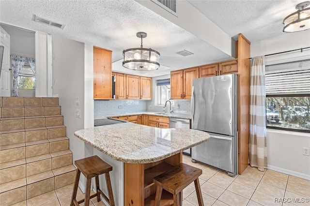 kitchen with decorative light fixtures, stainless steel appliances, a sink, light stone countertops, and a kitchen bar