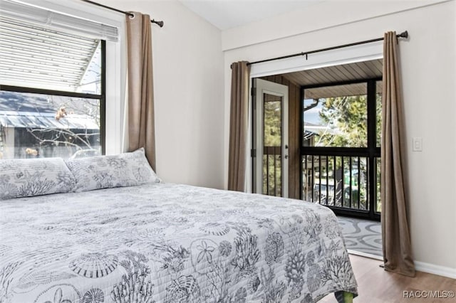 bedroom featuring access to outside, multiple windows, wood finished floors, and baseboards