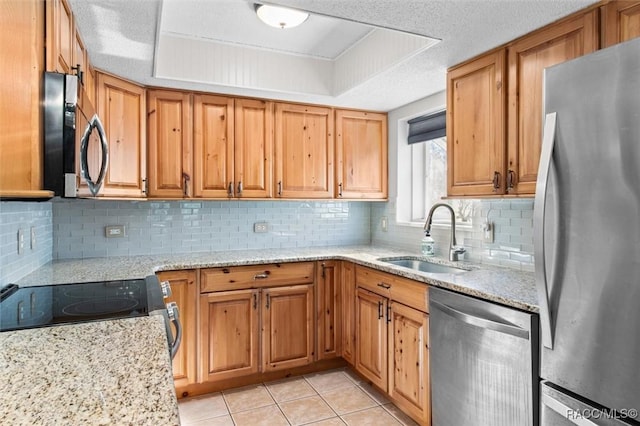 kitchen featuring stainless steel appliances, a tray ceiling, a sink, and light stone countertops