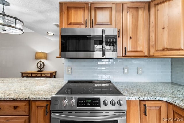 kitchen with appliances with stainless steel finishes, pendant lighting, and light stone counters