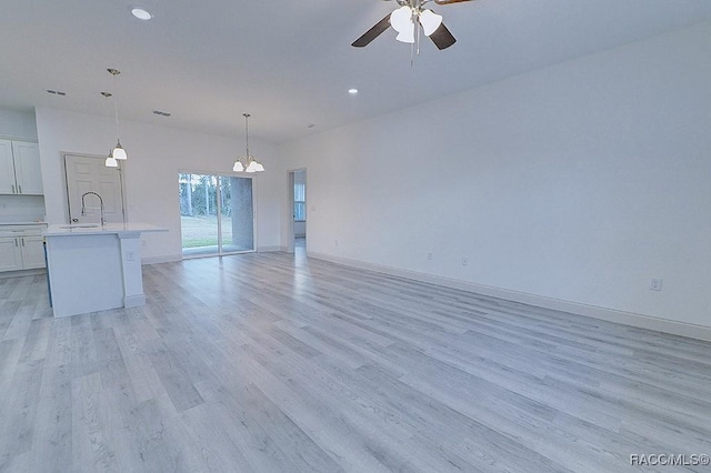 unfurnished living room with ceiling fan with notable chandelier, light hardwood / wood-style floors, and sink