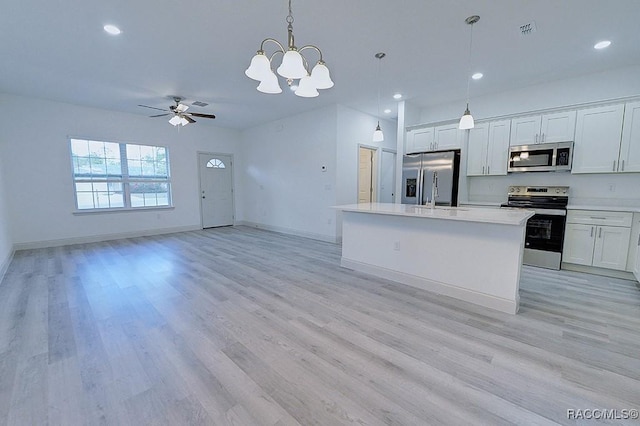 kitchen with a kitchen island with sink, ceiling fan with notable chandelier, hanging light fixtures, appliances with stainless steel finishes, and white cabinetry