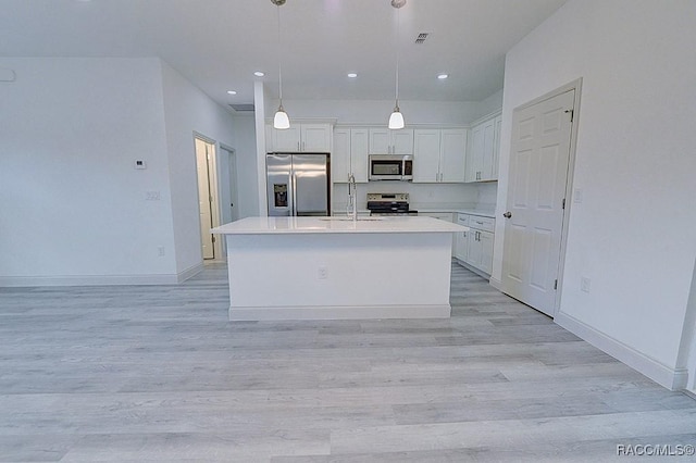 kitchen featuring stainless steel appliances, light hardwood / wood-style floors, decorative light fixtures, a center island with sink, and white cabinets