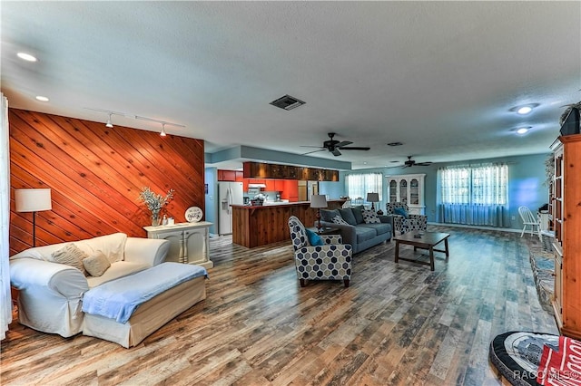 living room featuring a textured ceiling, track lighting, ceiling fan, and wood walls