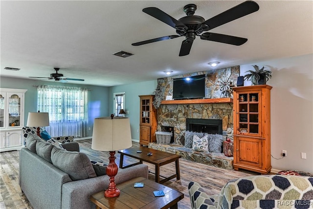 living room with a stone fireplace, ceiling fan, and light wood-type flooring