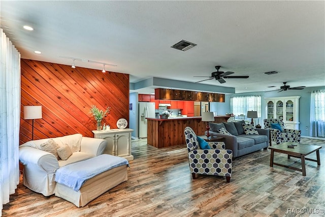 living room featuring a textured ceiling, wooden walls, ceiling fan, and track lighting