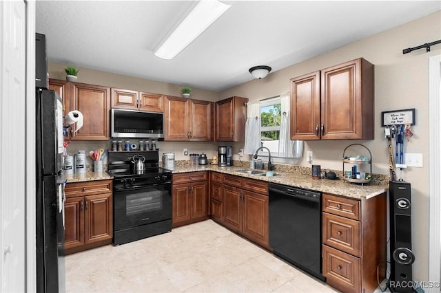 kitchen featuring a sink, brown cabinetry, black appliances, and light stone counters