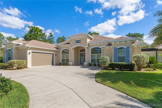 mediterranean / spanish-style home featuring a front lawn, driveway, an attached garage, and stucco siding