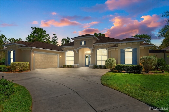 mediterranean / spanish house featuring an attached garage, a yard, concrete driveway, and stucco siding