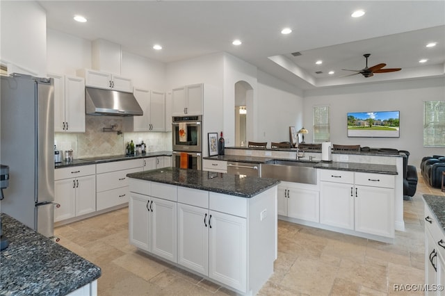 kitchen with appliances with stainless steel finishes, white cabinets, a kitchen island, and under cabinet range hood