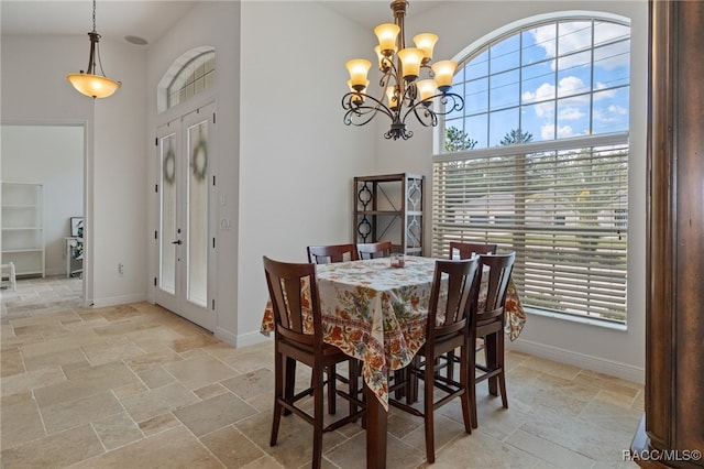 dining space featuring a chandelier, stone tile flooring, a towering ceiling, and baseboards