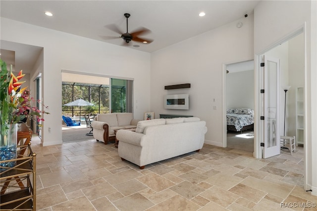 living room with stone tile flooring, ceiling fan, a towering ceiling, and baseboards