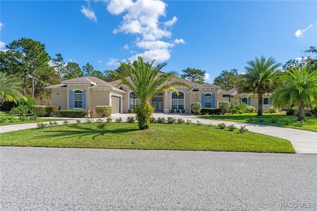 mediterranean / spanish-style house featuring a garage, concrete driveway, a front lawn, and stucco siding