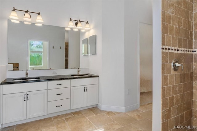 full bath with double vanity, baseboards, a sink, and tiled shower