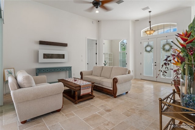 living area featuring a high ceiling, stone tile flooring, visible vents, and a ceiling fan