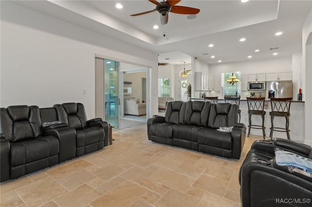 living room with a tray ceiling, a ceiling fan, stone tile flooring, and recessed lighting