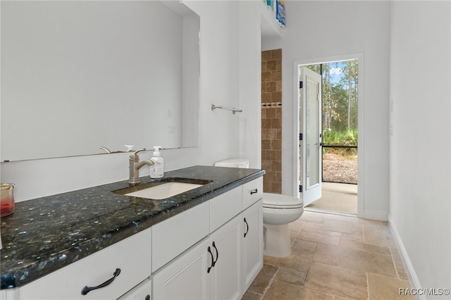 bathroom with stone tile flooring, baseboards, vanity, and toilet