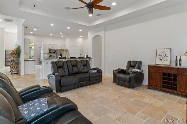 living area with arched walkways, recessed lighting, stone tile floors, visible vents, and a raised ceiling