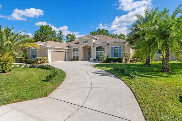 mediterranean / spanish house with a garage, concrete driveway, a front lawn, and stucco siding