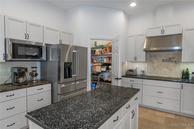 kitchen featuring stainless steel appliances, backsplash, stone finish flooring, white cabinetry, and under cabinet range hood