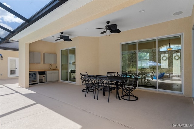 view of patio with outdoor dining area, a ceiling fan, a sink, exterior kitchen, and beverage cooler