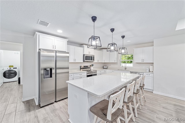 kitchen with a center island, white cabinets, sink, stainless steel appliances, and washer / clothes dryer