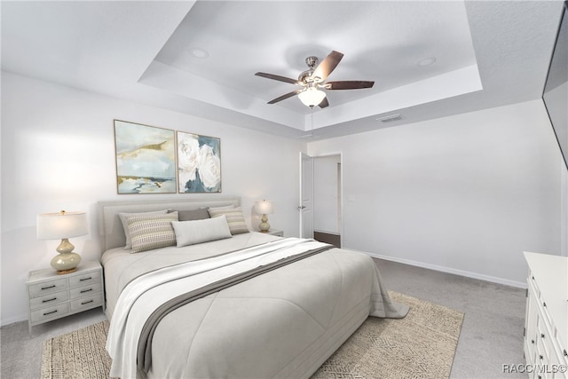 bedroom with light carpet, a raised ceiling, and ceiling fan